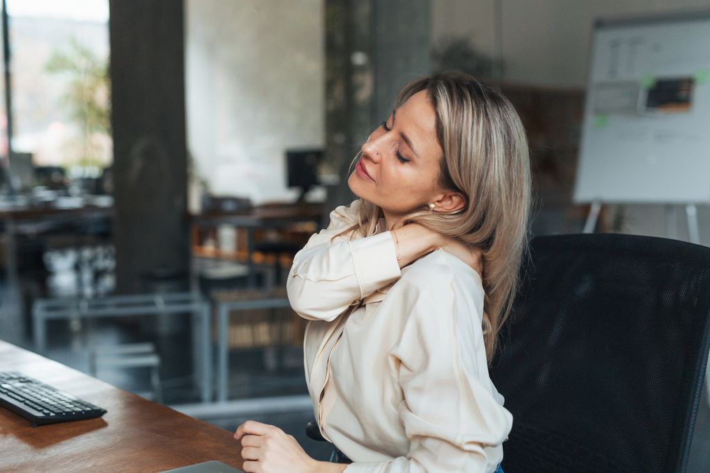 Businesswoman has stiffness in neck and shoulders from work at computer, tech neck or computer syndrome. Young female feeling under pressure, overworked spending long hours in office.